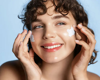 A person with a radiant complexion is shown smiling and applying a white nourishing cream to their face, which appears to be the LumiEssence C Nourishing Cream.